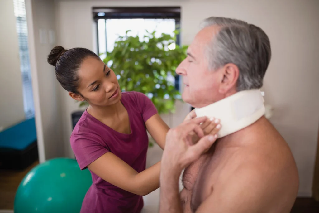 Female therapist examining neck collar of senior male patient