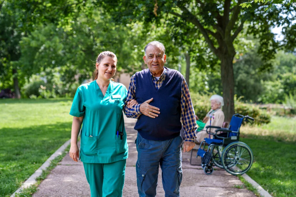 Elderly Man Assisted by Nurse in Sunny Nursing Home Garden