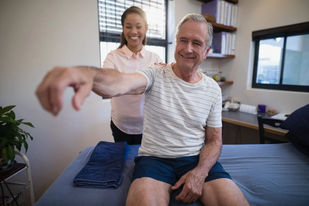 Smiling female doctor examining shoulder of senior male patient