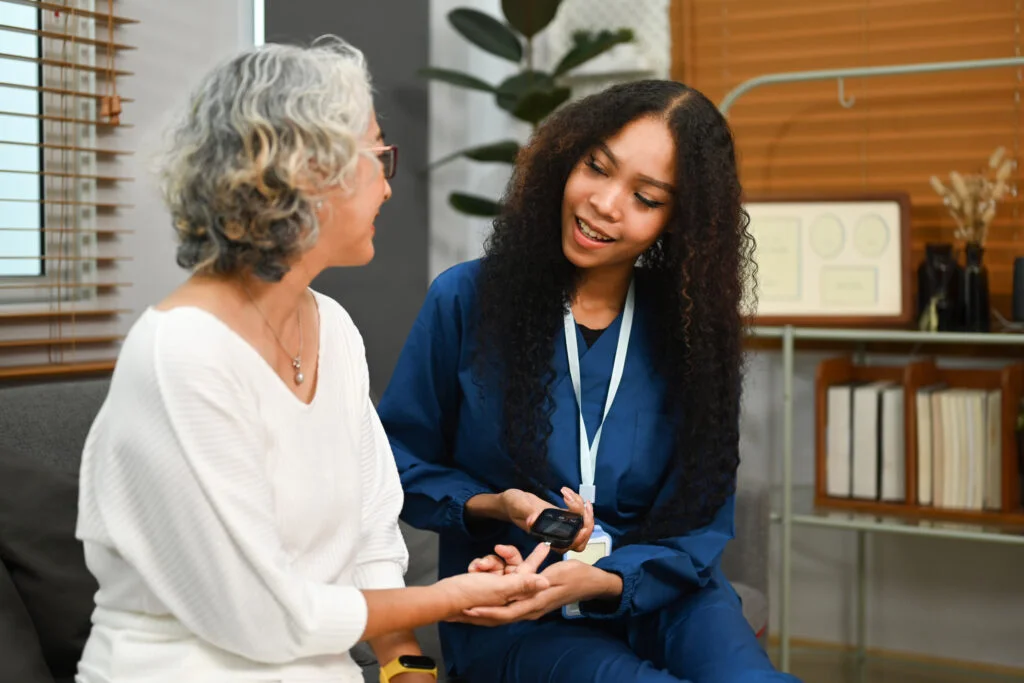 Smiling female caregiver checking blood glucose levels of senior