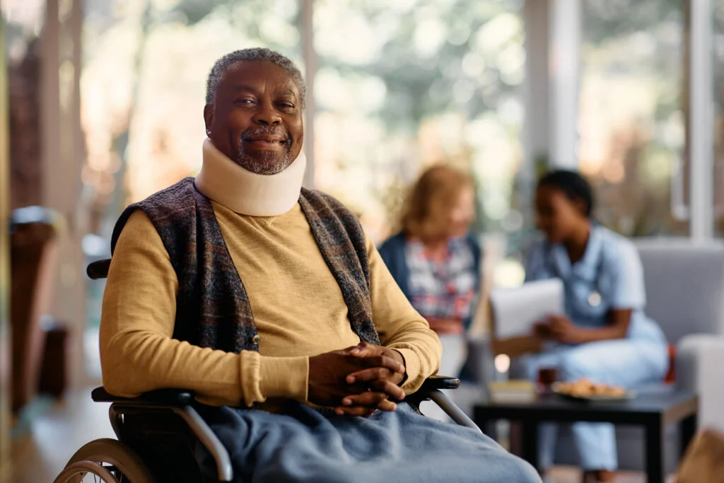 senior man in wheelchair wearing cervical collar while looking at camera.